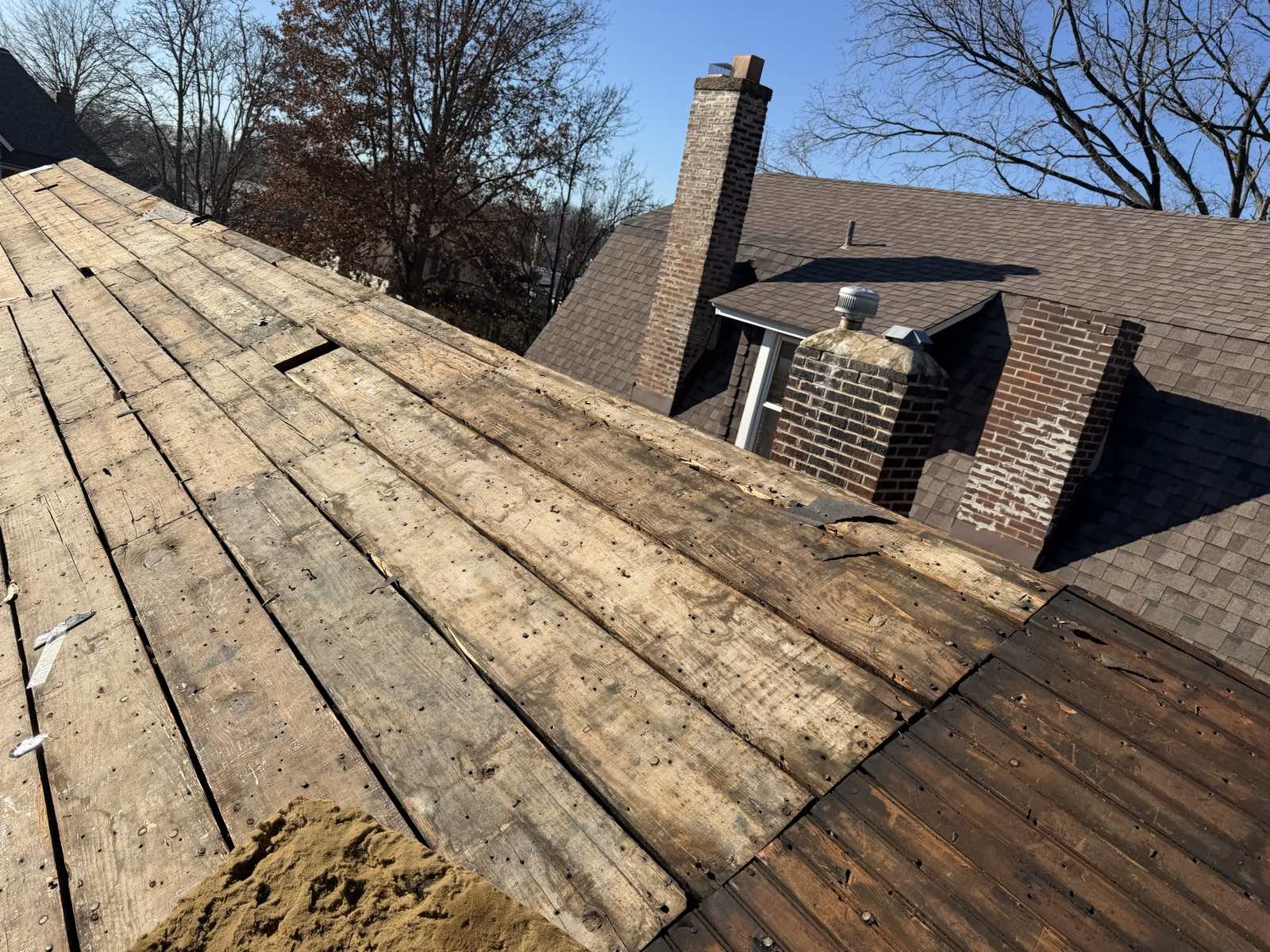 Bare plank decking exposed after a tear-off, with two brick chimneys and a neighbouring roof behind