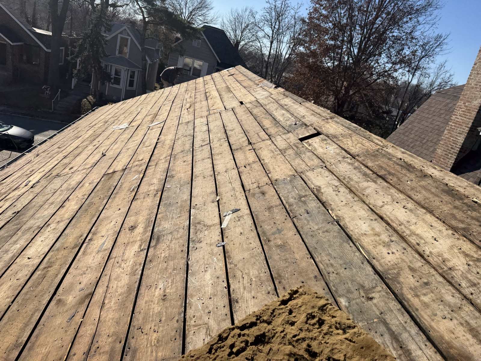 Bare plank roof decking exposed after a tear-off, with the street and neighbouring houses visible below