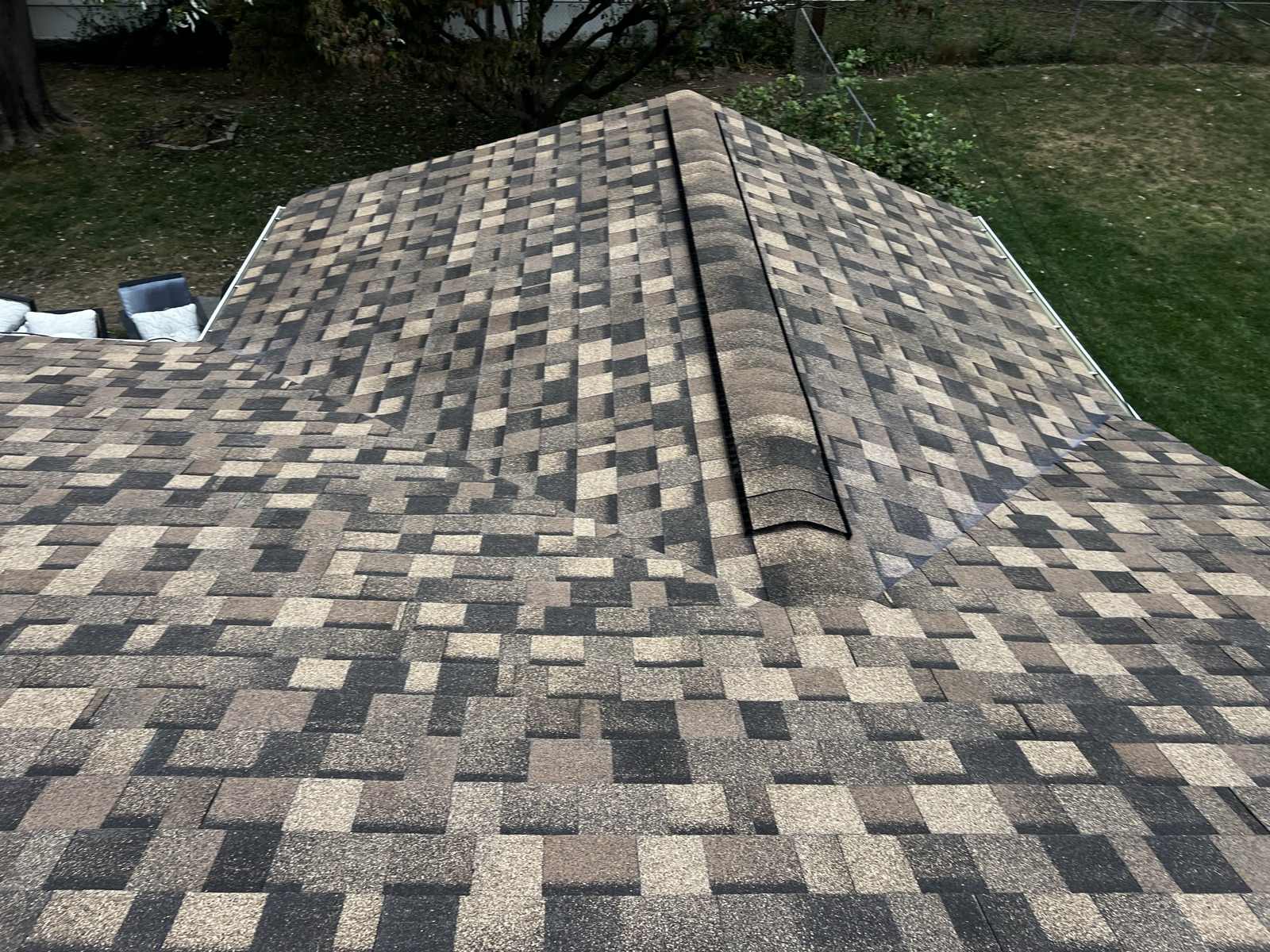 Newly laid multi-tone architectural shingles meeting at a hip, with ridge cap running along the top